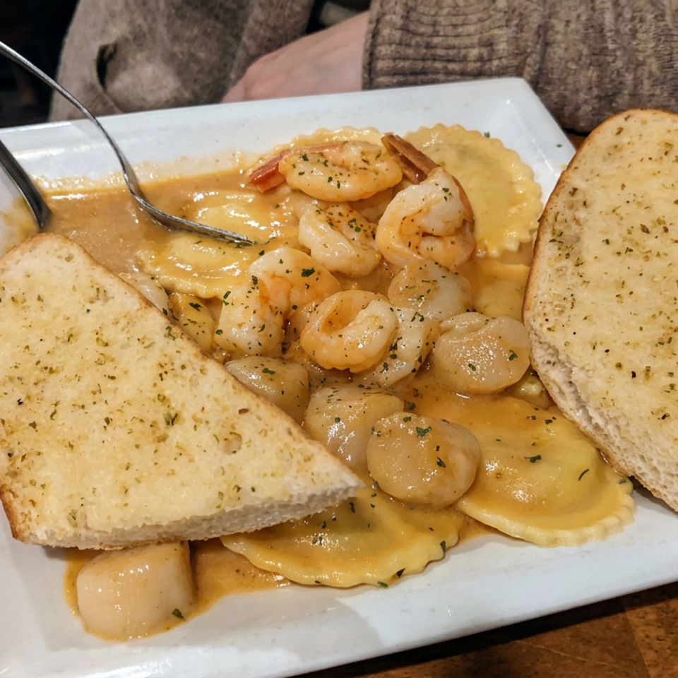 Plate of shrimp and ravioli in creamy sauce, served with garlic bread on a wooden restaurant table.