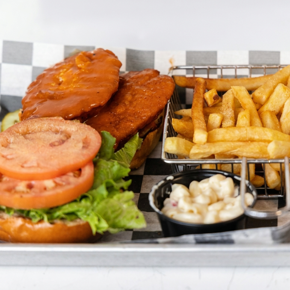 Burger with lettuce and tomato, barbecue chicken wings, fries, and dipping sauce on a checkered-lined metal tray.